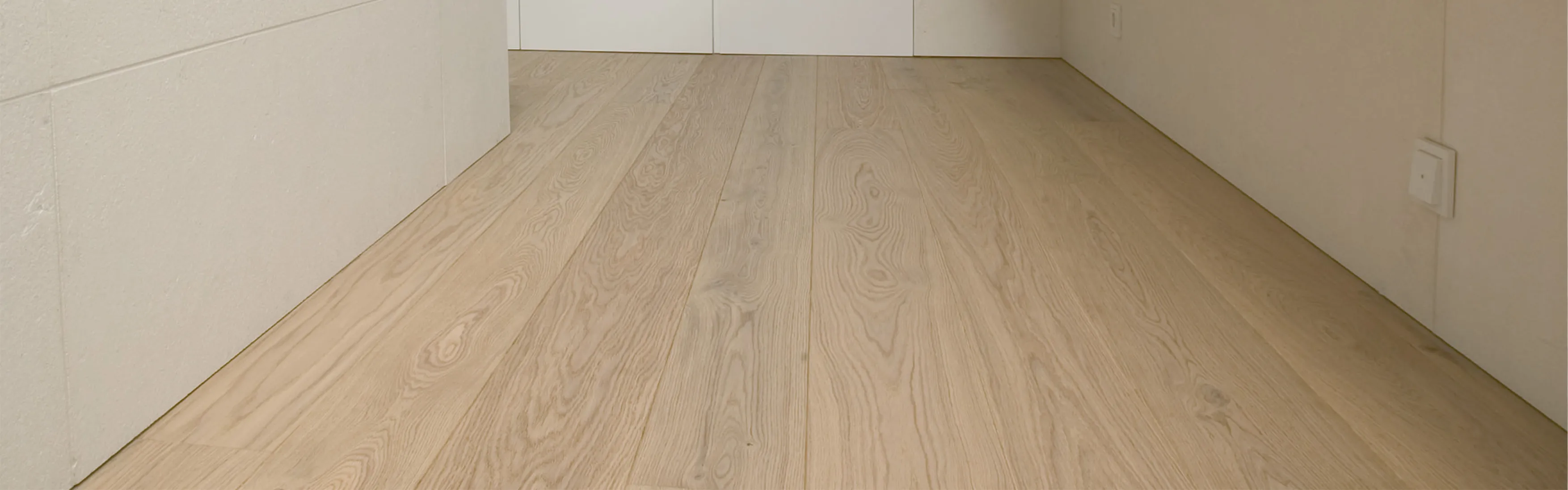 Ein heller Flur mit natürlichem Eichenparkett zieht sich entlang glatter, cremefarbener Wände. 