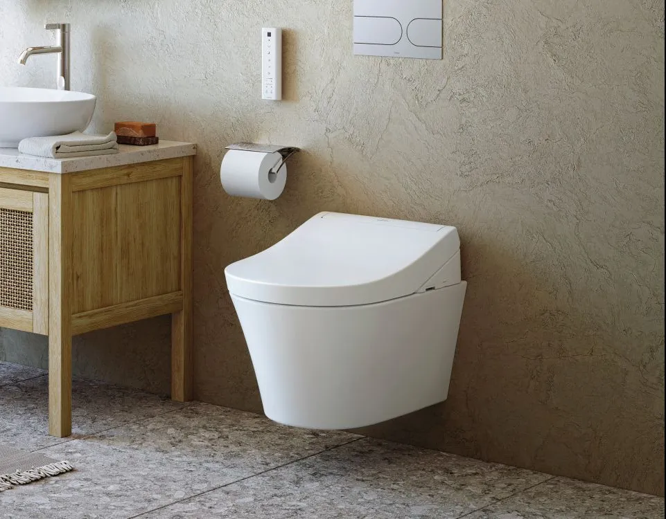 Ein TOTO WASHLET RG hängt an einer hellen Wand, daneben ein Holzunterschrank mit rundem Aufsatzwaschbecken und Spiegel.