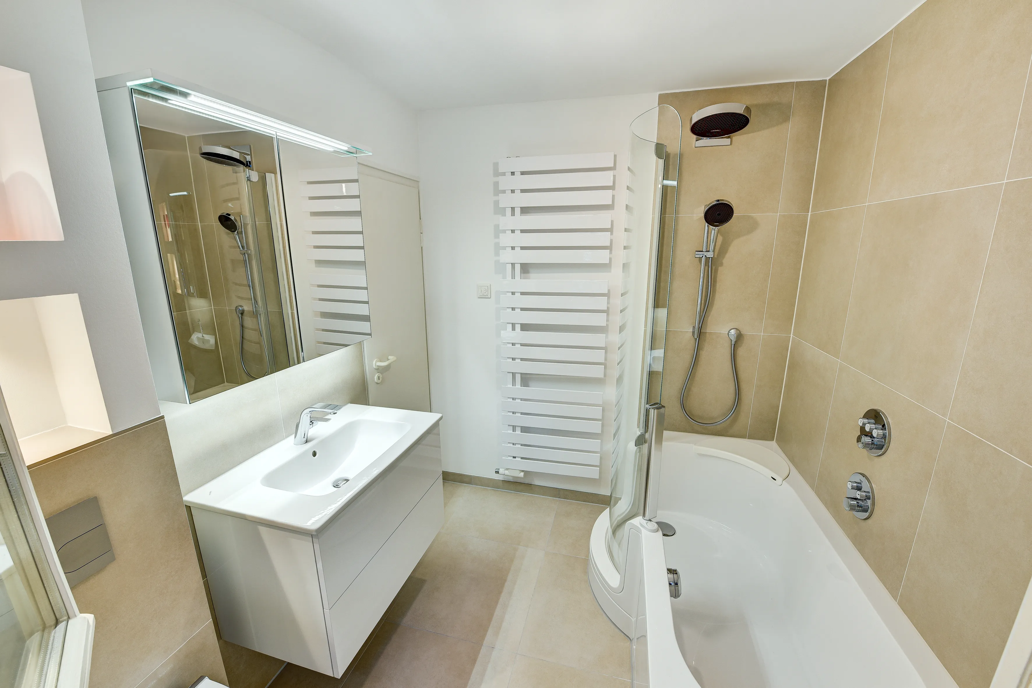 Badezimmer mit Badewanne, integrierter Duschabtrennung und Handbrause vor hellen Wandfliesen, umgesetzt von der Nessmann Bad & Heizung GmbH.