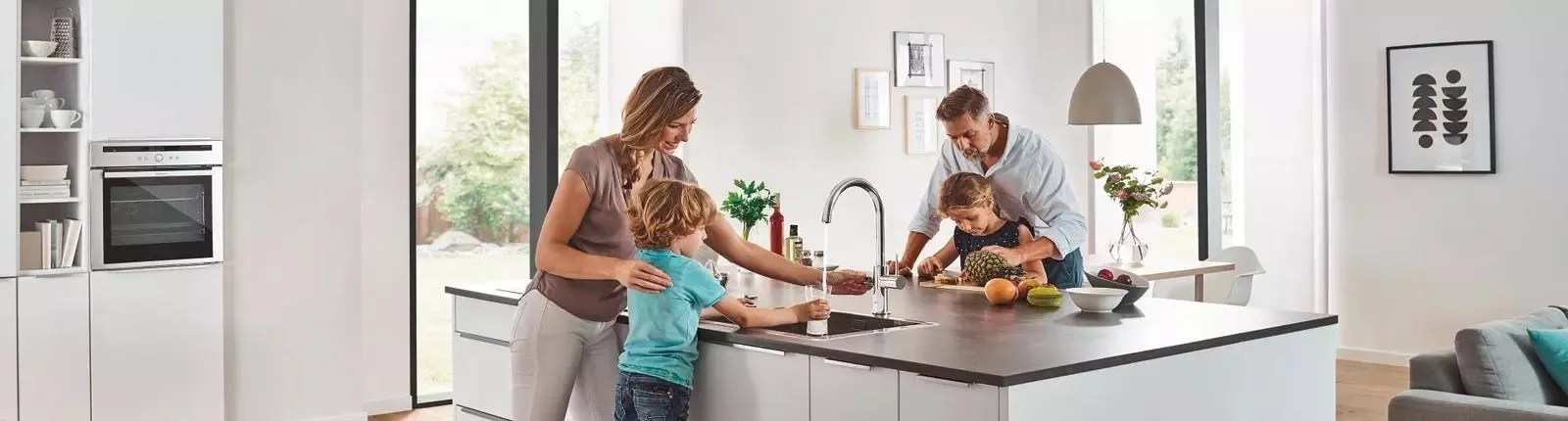 Familie nutzt moderne Küchenarmatur mit Trinkwassersystem Grohe Blue in heller, offener Wohnküche.