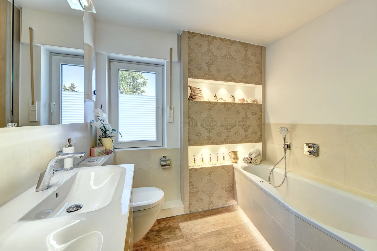 Helles Badezimmer mit Waschtisch, WC, Badewanne und beleuchteten Wandnischen, umgesetzt von der Nessmann Bad & Heizung GmbH.
