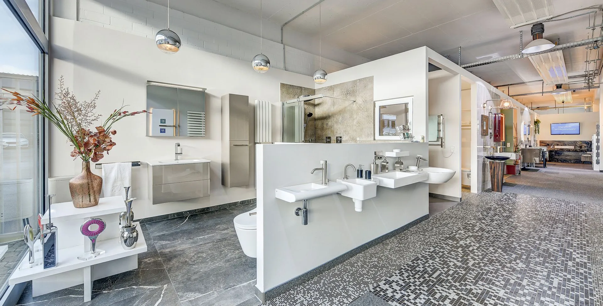 Eine moderne Badausstellung der Nessmann bad & heizung GmbH zeigt stilvolle Waschbecken, Armaturen und Duschen in einem hellen, offenen Raum mit eleganter Einrichtung.