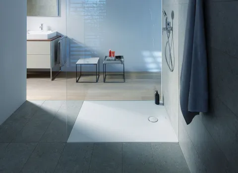 Ein stilvolles Badezimmer mit einer flachen Duschwanne, umgeben von Glaswänden und grauen Fliesen. 