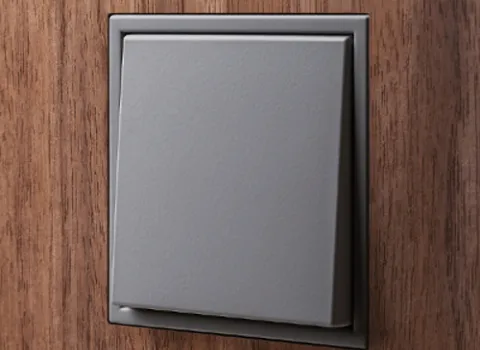 Nahaufnahme flächenbündig in Holzwand integrierter grauer Lichtschalter der Serie LS Zero von JUNG..