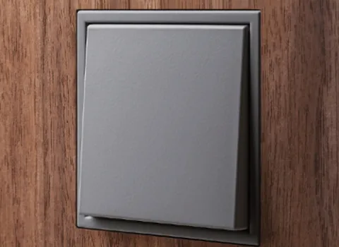 Nahaufnahme flächenbündig in Holzwand integrierter grauer Lichtschalter der Serie LS Zero von JUNG..