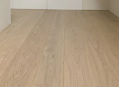 Ein heller Flur mit natürlichem Eichenparkett zieht sich entlang glatter, cremefarbener Wände. 