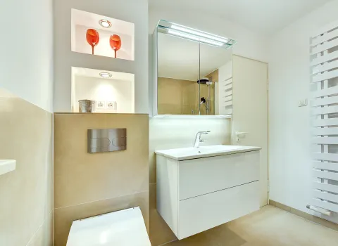 Kompakter Badbereich mit beleuchtetem Spiegelschrank, Waschtisch und integrierten Wandnischen, realisiert durch die Nessmann Bad & Heizung GmbH.