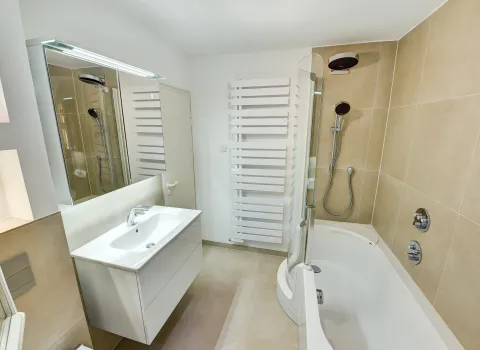 Badezimmer mit Badewanne, integrierter Duschabtrennung und Handbrause vor hellen Wandfliesen, umgesetzt von der Nessmann Bad & Heizung GmbH.