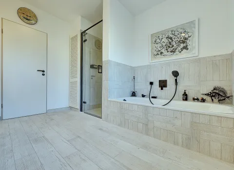 Großzügiger Badbereich mit integrierter Badewanne, Glasdusche und dekorativer Wandgestaltung, ausgeführt von der Nessmann Bad & Heizung GmbH.