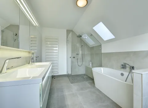 Großzügiges Dachbad mit Doppelwaschbecken, Walk-In-Dusche und Badewanne unter dem Dachfenster, gestaltet von der Nessmann Bad & Heizung GmbH.