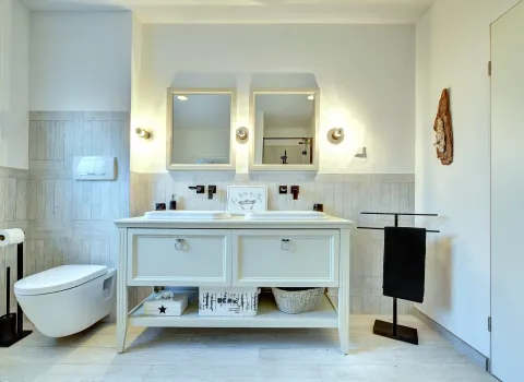 Klassisch gestaltetes Badezimmer mit Doppelwaschtisch, zwei Wandspiegeln und wandhängendem WC, geplant von der Nessmann Bad & Heizung GmbH.