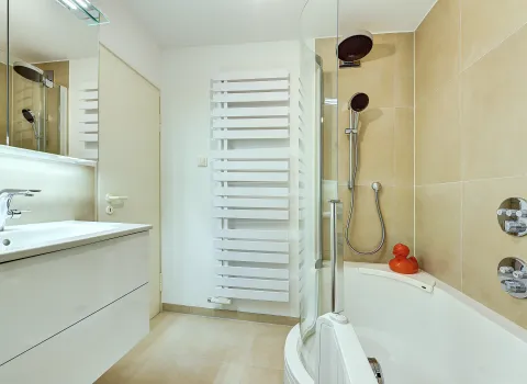 Badezimmer mit Badewanne, integrierter Duschabtrennung und Handbrause vor hellen Wandfliesen, umgesetzt von der Nessmann Bad & Heizung GmbH.