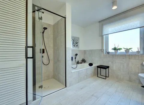 Modernes Bad mit schwarzer Armatur, bodengleicher Dusche und Badewanne vor hell gefliesten Wänden, umgesetzt durch die Nessmann Bad & Heizung GmbH.