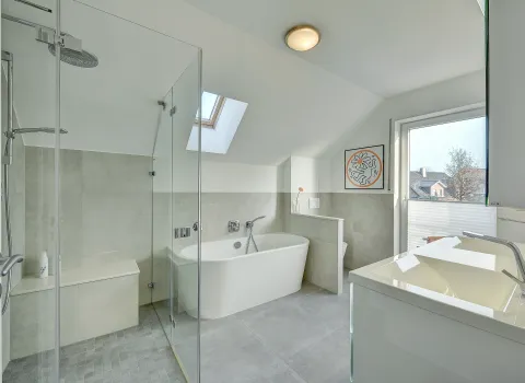Modernes Badezimmer mit bodengleicher Glasdusche, freistehender Badewanne und Dachfenster, realisiert von der Nessmann Bad & Heizung GmbH.