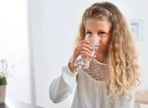Mädchen trinkt ein Glas frisches, gefiltertes Trinkwasser aus der Küche.