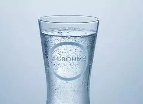 Sprudelndes Trinkwasser im Glas mit Grohe Blue Logo vor hellem Hintergrund.