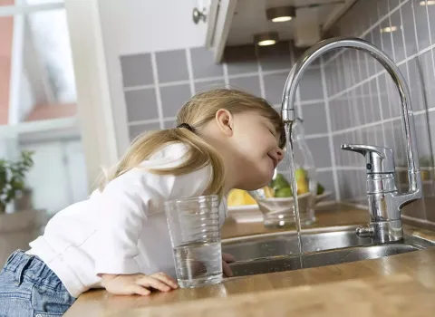 Kind trinkt gefiltertes Trinkwasser direkt aus der Grohe Blue Küchenarmatur.