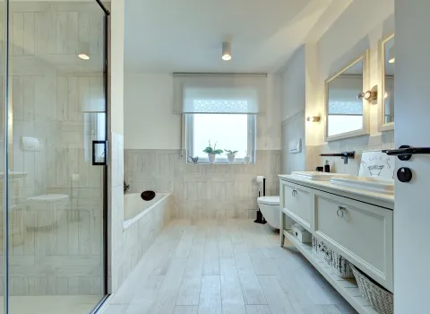 Helles Badezimmer mit bodengleicher Glasdusche, eingelassener Badewanne und Waschtischmöbel in Holzoptik, realisiert von der Nessmann Bad & Heizung GmbH.