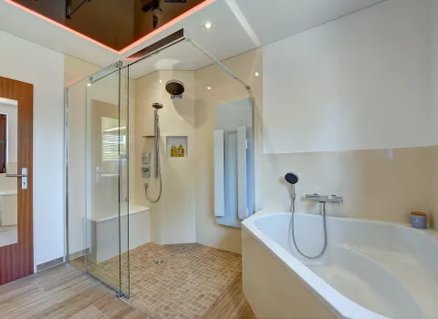 Blick auf bodengleiche Dusche mit Glasabtrennung und angrenzende Badewanne in einem modern gestalteten Badezimmer der Nessmann Bad & Heizung GmbH.