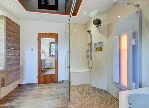 Detailansicht der bodengleichen Dusche mit Glaswand, Sitzbank und vertikal montierter Infrarotheizung der der Nessmann Bad & Heizung GmbH.