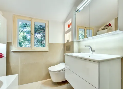 Helles Bad mit wandhängendem WC, Waschtischunterschrank und Fensterblick ins Grüne, realisiert von der Nessmann Bad & Heizung GmbH.