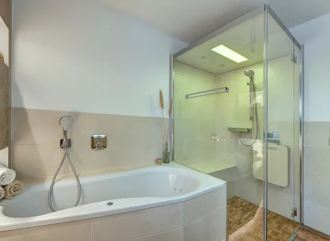 Kombination aus Badewanne und bodengleicher Glasdusche mit integrierter Sitzbank in einem modern gestalteten Badezimmer der Nessmann Bad & Heizung GmbH.