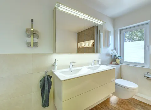 Moderner Doppelwaschtisch mit Spiegelschrank, Wand-WC und Tageslichtfenster, realisiert von der Nessmann Bad & Heizung GmbH.