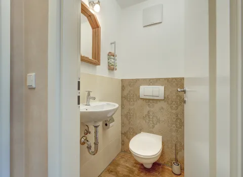 Kompaktes Gäste-WC mit wandhängender Toilette, kleinem Waschtisch und dekorativer Wandgestaltung von der Nessmann Bad & Heizung GmbH.