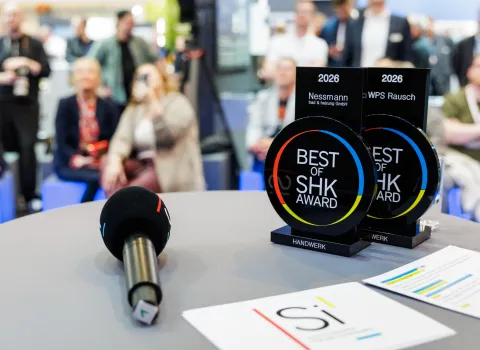 Zwei schwarze „Best of SHK Award 2026“-Trophäen stehen auf einem runden Tisch neben einem Mikrofon und mehreren Unterlagen.