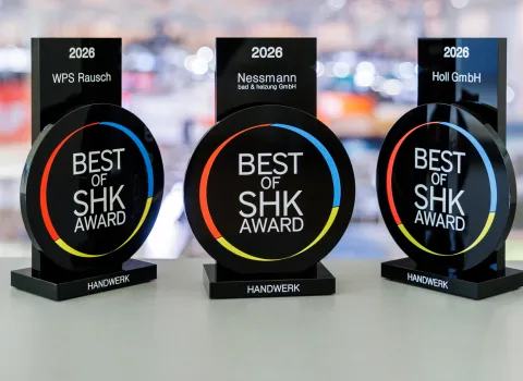 Drei schwarze „Best of SHK Award 2026“-Trophäen stehen nebeneinander auf einer hellen Fläche vor einem unscharfen Messehintergrund.