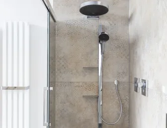 Eine moderne Dusche mit großer Regenbrause, Glasabtrennung und stilvollen, beigen Fliesen mit feinen Mustern der Nessmann bad & heizung GmbH.