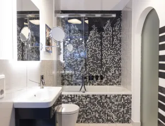 Ein modernes Badezimmer mit einer stilvollen Badewanne, einem Waschbecken mit Spiegel und schwarz-weißen Mosaikfliesen, Teil der Ausstellung in Düsseldorf von Nessmann bad & heizung GmbH.