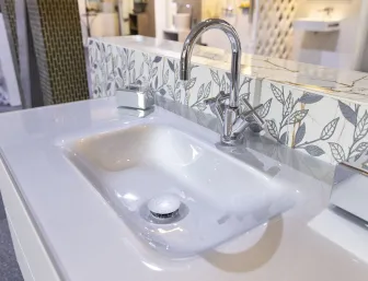 Ein elegantes Waschbecken mit glänzender, geschwungener Armatur und dekorativen Fliesen mit Blättermuster, ausgestellt in Düsseldorf von Nessmann bad & heizung GmbH.