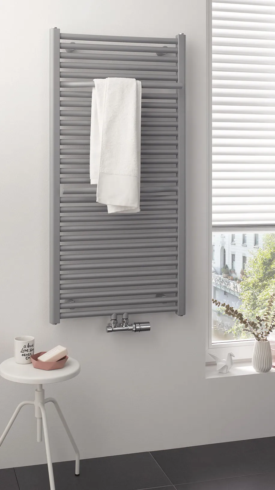 In einem hellen Badezimmer hängt ein grauer HSK Line Plus Heizkörper mit einem weißen Handtuch daran. 