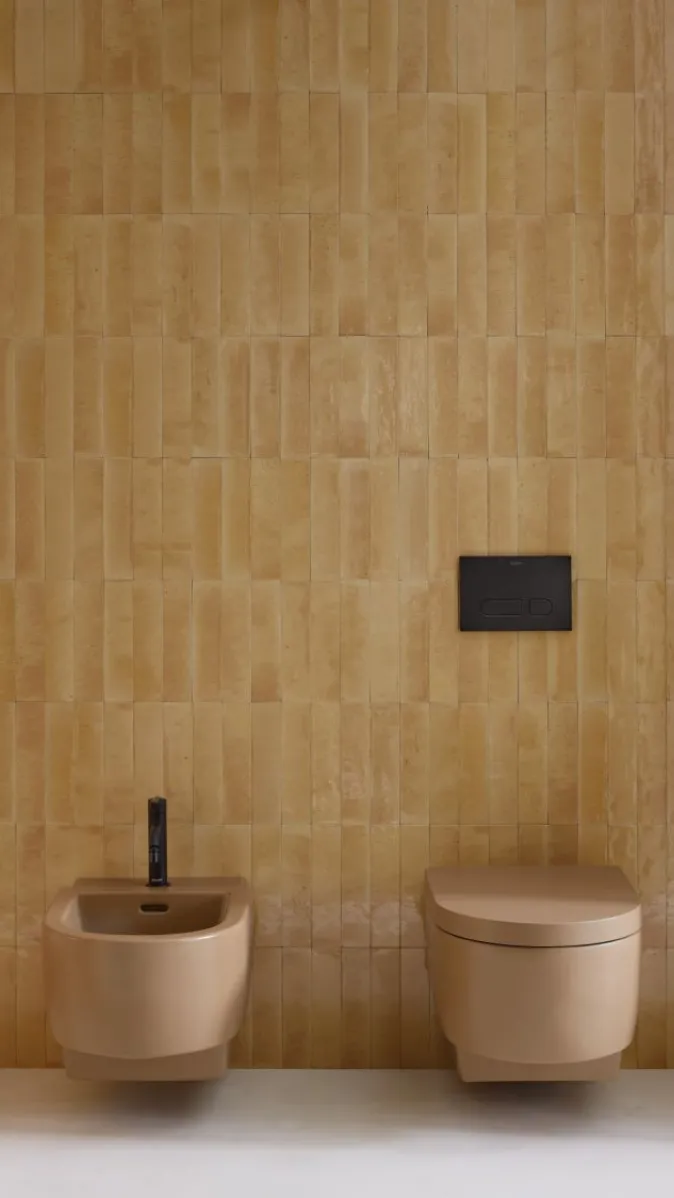 WC und Bidet der Serie Balcoon von Duravit in Schwarz vor einer goldbraun gefliesten Wand.